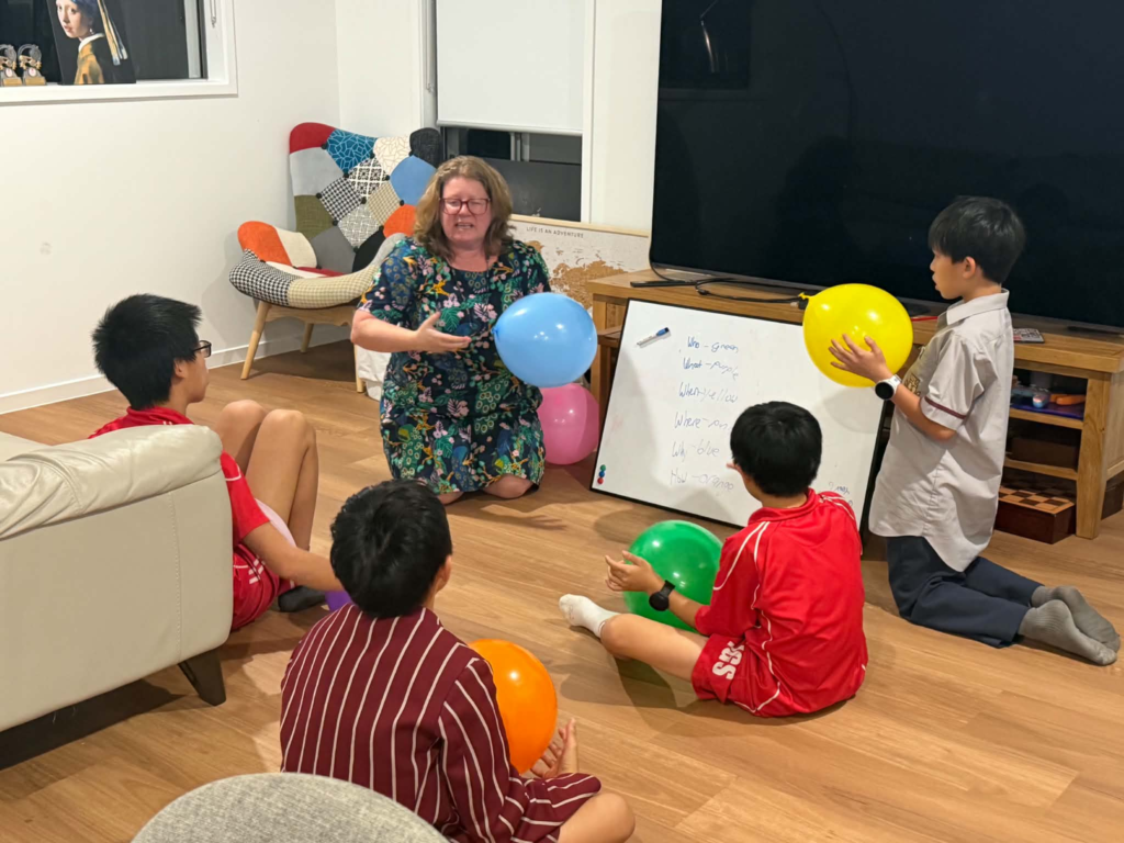 Yasmin leading a classroom balloon activity with students, colour-coded for a Who, What, When, Where, Why and How game